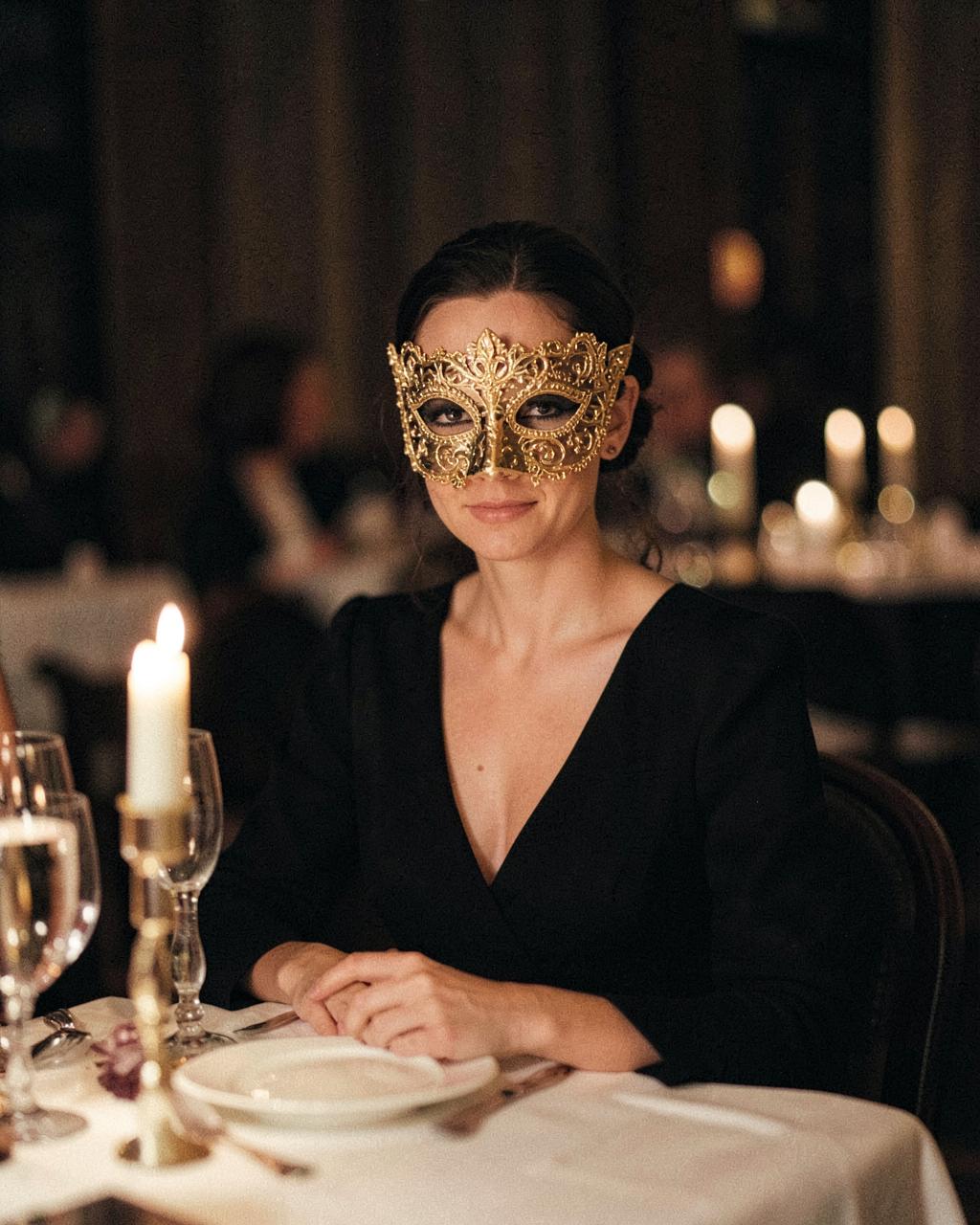 Vrouw in avondjurk met Venetiaans halfmasker aan tafel