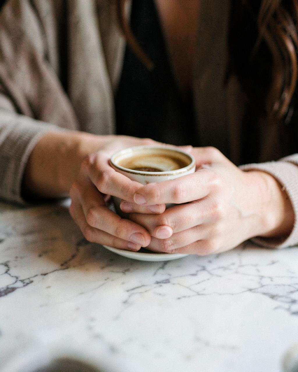 Handen rond een kop koffie op een marmeren tafel