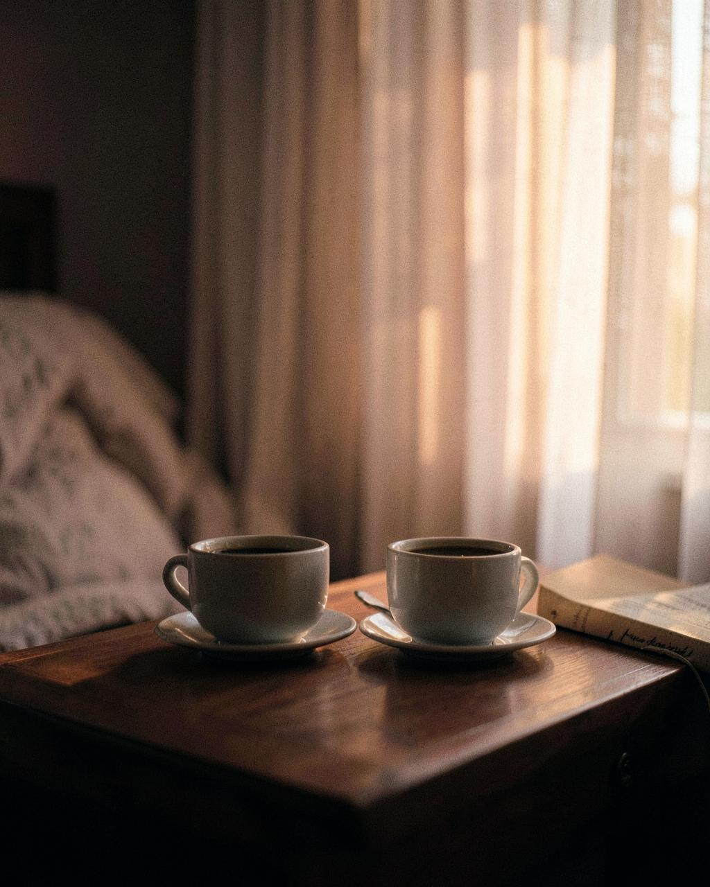 Twee koffiekoppen op een nachtkastje bij zonsopgang